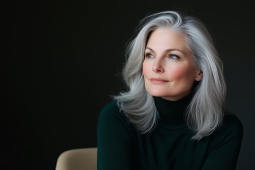 Thoughtful silver-haired woman in turtleneck seated in modern chair with subtle lighting in dark minimalist room photo