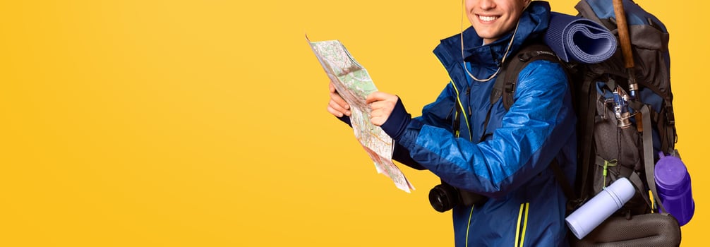 Happy man backpacker following map, smiling over orange background, side view photo