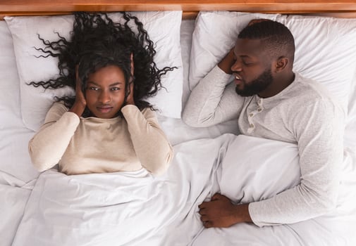Annoying snoring. Young black woman closing ears with hands suffering from loud snore of her sleeping husband. photo