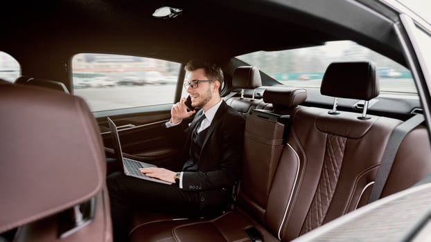 Excited businessman with laptop receiving a phone call in the back seat of luxury car, working photo