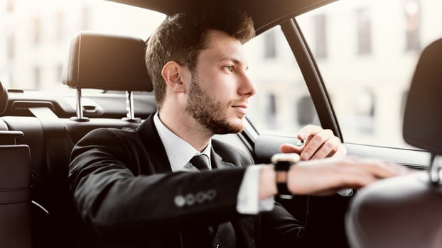 Young handsome bearded businessman in suit sitting in luxury car, looking out of window at city photo
