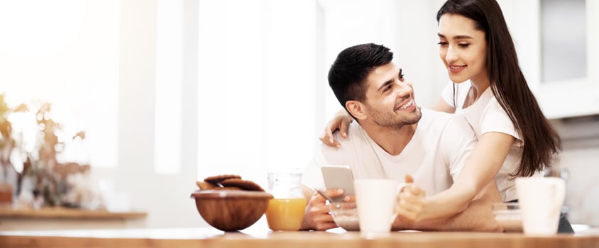 Relationship Concept. Cheerful european family spending time together in kitchen, using smart phone, having coffee photo