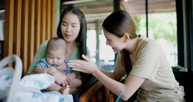 Selective focus, Two women share a joyful moment in a coffee shop, smiling as they engage with a baby boy sitting on one woman's lap. Family enjoying time together. photo