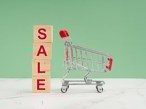 A miniature shopping trolley and wooden blocks with the word SALE over a blue background photo