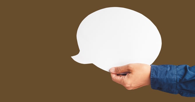 Close-up of hand holding a white speech bubble against a brown background photo