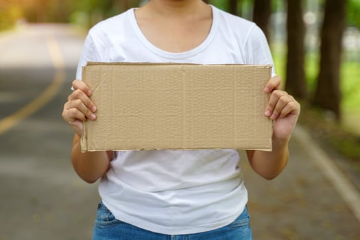 Young Asian woman wearing white t-shirt stands and holds up a brown cardboard sign with space for writing. Concept of campaign sign, advertisement, protest. photo