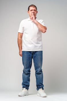 A man makes a playful gesture with his hand near his mouth while smiling in a neutral backdrop photo