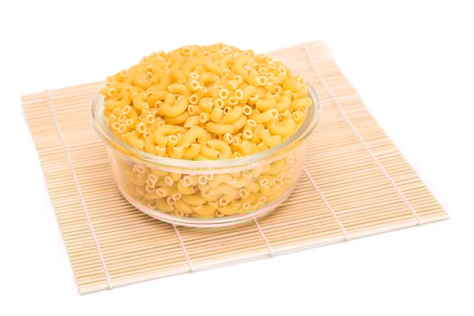 Uncooked Chifferi Rigati Pasta in Glass Jar on Bamboo Mat Isolated White Background. Fat and Unhealthy Food. Classic Dry Macaroni. Italian Culture and Cuisine. Raw Pasta - Isolation photo