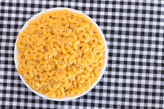 Uncooked Chifferi Rigati Pasta in White Cup on Black Checkered Towel. Fat and Unhealthy Food. Classic Dry Macaroni. Italian Culture and Cuisine. Raw Pasta photo