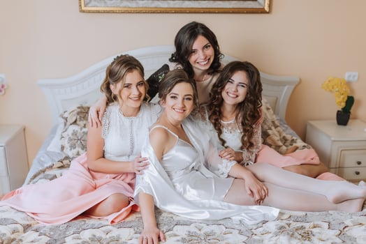 Four women are sitting on a bed, smiling and hugging each other photo