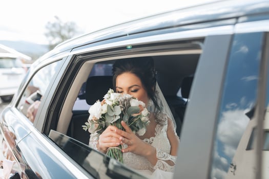A bride is getting into a car with a bouquet of flowers photo