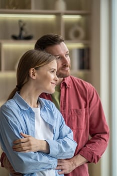 Calm relaxed married couple standing with gentle embrace looking to window together enjoys slow life photo