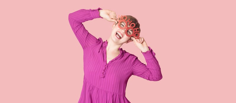 A cheerful young woman in Christmas glasses poses on a highlighted pink background. photo