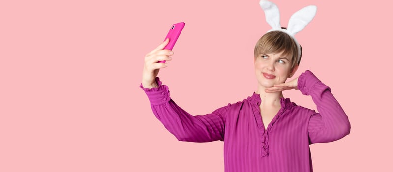 A beautiful girl with bunny ears on a colored background with a smartphone in her hands. photo