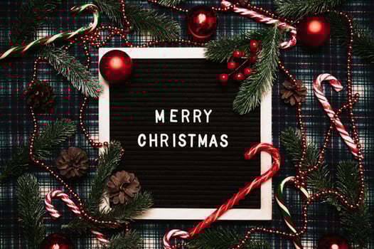 Merry Christmas lettering in plastic letters on an old vintage letter board. There are caramel canes, balls, cones and fir branches all around. Top view. Flatley. Ready-made Christmas greeting card. photo