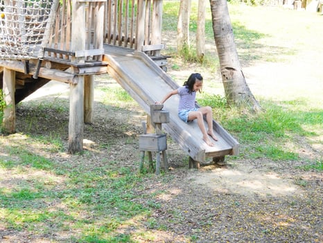 Children play outdoors on a wooden playground in a park. Happy girl playing on slide in playground in summer. photo