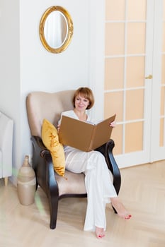An adult beautiful woman spends time in her stylish living room and holds a big book in her hands. photo