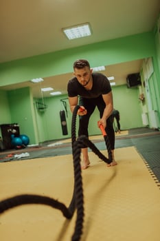 A fit athlete man doing intense battle rope exercise at crossfit gym. photo