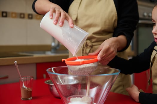 Mother and child sifting flour for baking in home kitchen photo