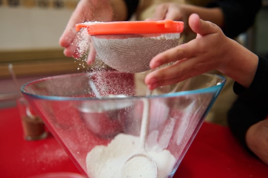 Hands sifting flour into a glass bowl on a kitchen counter photo
