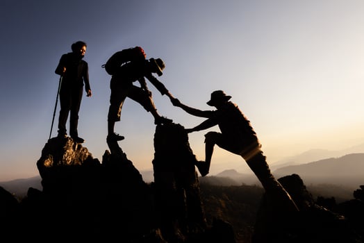 Silhouette of Hikers climbing up mountain cliff. Climbing group helping each other while climbing up in sunset. Concept of help and teamwork. photo