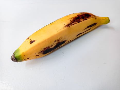 Ripe banana with brown spots on white background photo