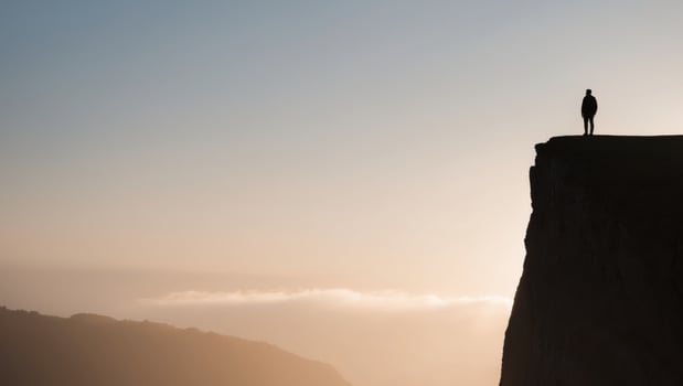 Silhouette of a man standing on the edge of a cliff at sunset photo