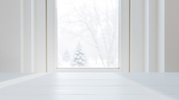 white wooden surface bathed sunlight with a snowy view through the window photo