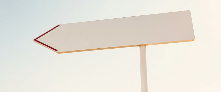 white arrow sign points left against a light blue sky photo