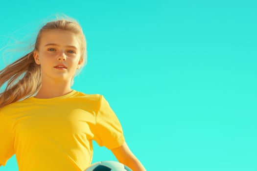 Determined young girl in yellow uniform kicks soccer ball in bright stadium under clear sky photo