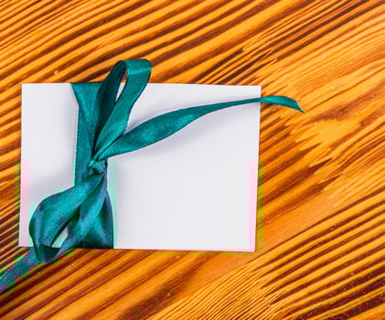 Blank note with green ribbon left on wooden board, concept photo