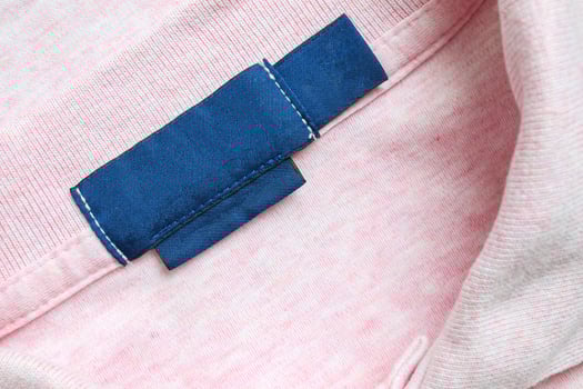 Blank blue laundry care clothes label on pink shirt fabric texture background photo