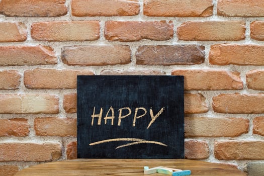 Chalk board with the word HAPPY drown by hand and chalks on wooden table on brick wall background. photo