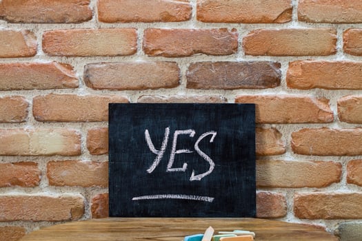 Chalk board with the word YES drown by hand and chalks on wooden table on brick wall background. photo