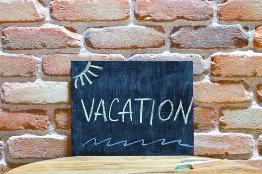 Chalk board with the word VACATION drown by hand and chalks on wooden table on brick wall background. photo