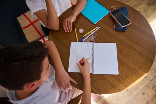 Top view of children doing homework at wooden table with notebooks photo
