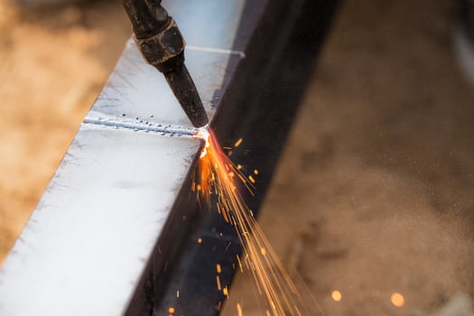 Skilled welder cuts metal with a gas torch in industrial workshop. Sparks fly during precision fabrication process. Craftsman control and expertise in metalworking. Gas torch cuts through steel. photo