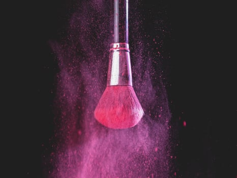 Make-up brush with pink powder splashes explosion on black background. Beauty concept photo