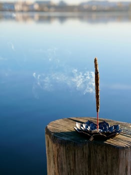 A small incense stick sitting on a wooden post near a lake photo
