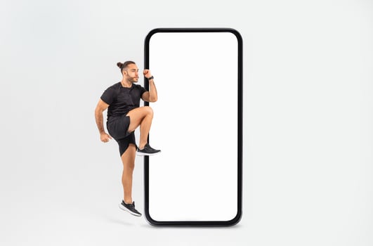 A man is playfully stepping up against a large blank smartphone display, showcasing an energetic pose. The indoor environment is simple and bright, emphasizing his enthusiasm. photo