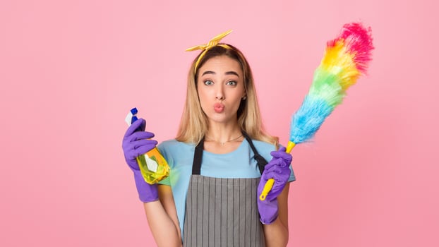 Cleaning at home from dust concept. Housewife makes blowing kiss and holds in hands multi-colored brush and spray photo