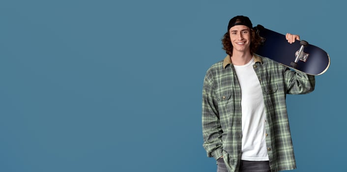 Teenage outdoor activities. Happy young guy holding skateboard on color background photo