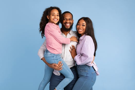 Love And Care. Portrait of smiling African American mum and dad hugging, guy carrying holding daughter on hands standing isolated on blue studio background. Cheerful man and woman posing with girl photo