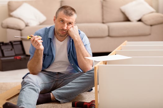 Unhappy Man Assembling Furniture Himself Having Trouble Installing Cabinet Sitting On Floor At Home. Copy Space photo