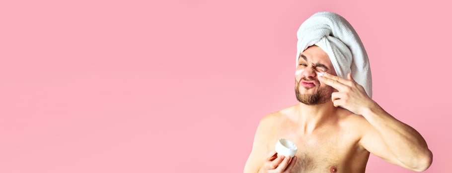 Cute young man grimacing and smears face cream isolated. On pink background photo