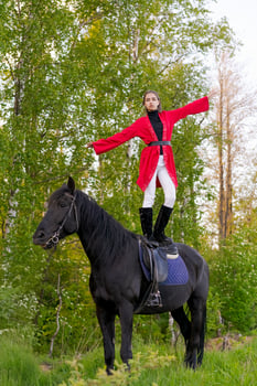 Woman is standing on top of a black horse in a forest photo
