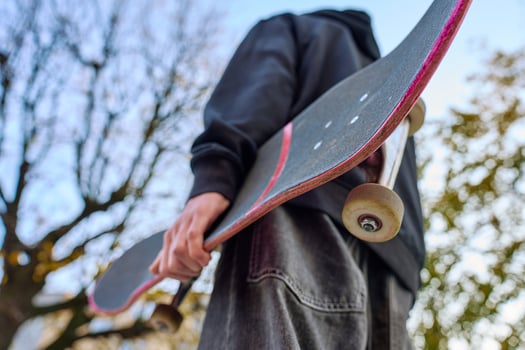 Skateboarder holding worn skateboard walks at street photo