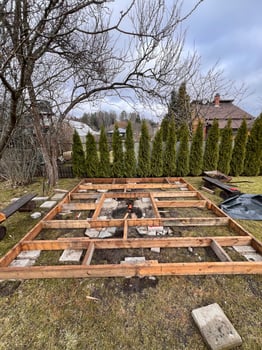 Framework of a wooden deck under construction in a backyard with trees and greenery in the background. photo