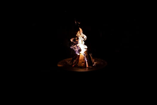 Solitary Campfire in Circular Metal Fire Pit Against Black Background photo