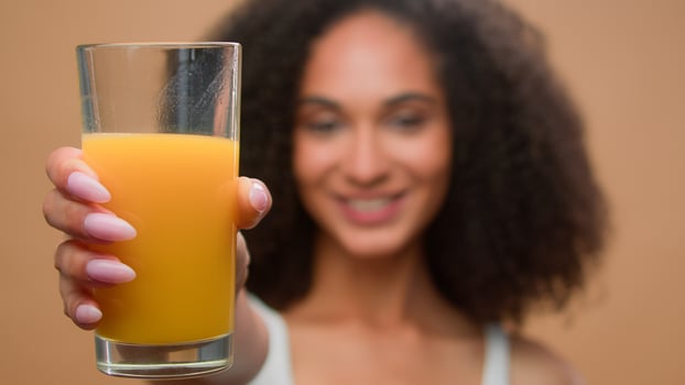Happy healthy African American woman ethnic girl female model drinking fresh orange juice vitamin drink stretch hand with glass motivate clink clinking suggest to try diet detox health care in studio photo